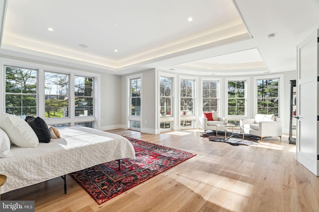 bedroom with light wood-style flooring, baseboards, a raised ceiling, and recessed lighting