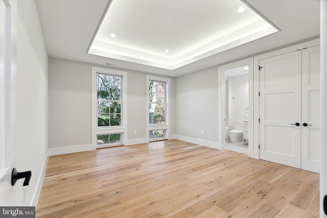 empty room featuring light wood-style floors, baseboards, and a raised ceiling