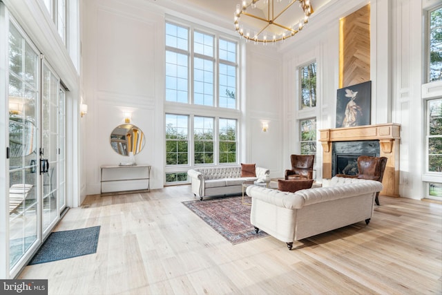 living area with a premium fireplace, wood finished floors, a towering ceiling, and a notable chandelier