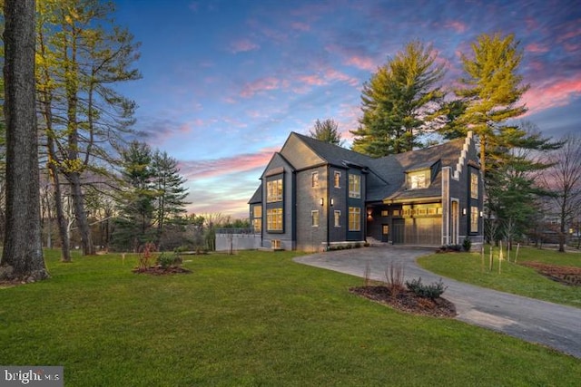 back of property at dusk featuring a garage, driveway, and a lawn