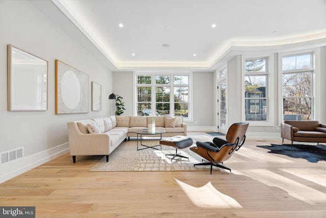 living room with a tray ceiling, light wood-type flooring, visible vents, and recessed lighting