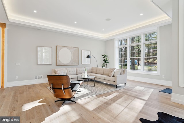 living room featuring a tray ceiling, baseboards, visible vents, and light wood finished floors