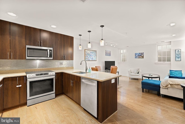 kitchen with appliances with stainless steel finishes, open floor plan, light countertops, light wood-style floors, and a sink