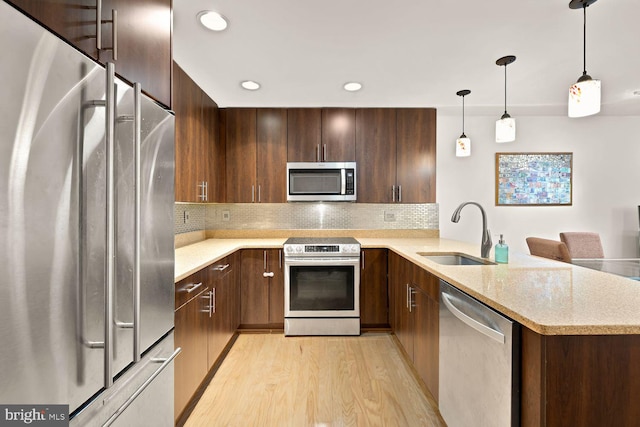 kitchen featuring tasteful backsplash, light wood-style flooring, appliances with stainless steel finishes, a peninsula, and a sink