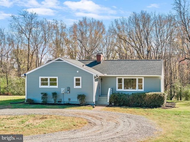 ranch-style home featuring driveway, a shingled roof, a chimney, and a front lawn