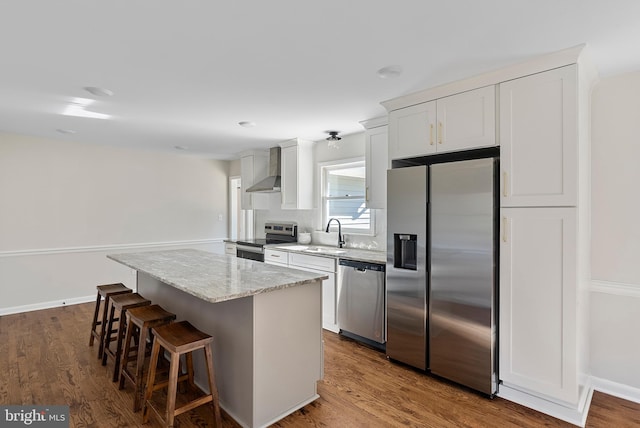 kitchen with white cabinets, wall chimney exhaust hood, a kitchen island, wood finished floors, and stainless steel appliances