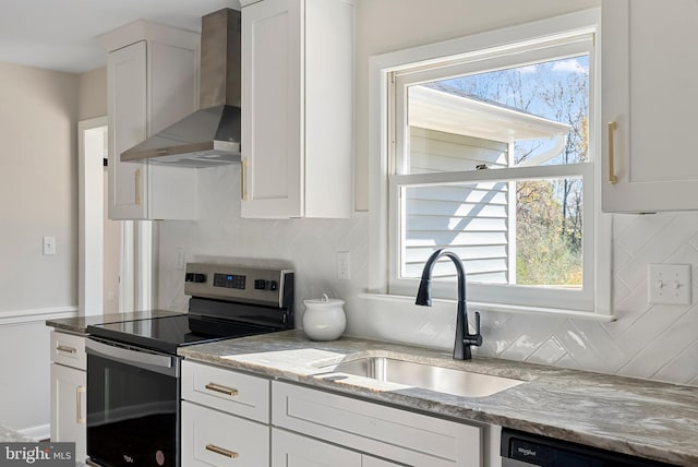 kitchen featuring light stone counters, a sink, white cabinets, wall chimney range hood, and appliances with stainless steel finishes