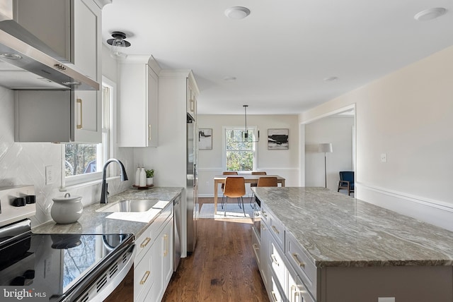 kitchen with dark wood finished floors, wall chimney range hood, light stone countertops, stainless steel range with electric stovetop, and a sink