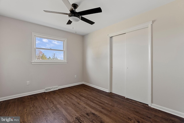 unfurnished bedroom featuring a ceiling fan, visible vents, baseboards, a closet, and dark wood finished floors