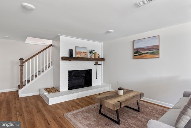 living area featuring baseboards, visible vents, stairway, wood finished floors, and a brick fireplace