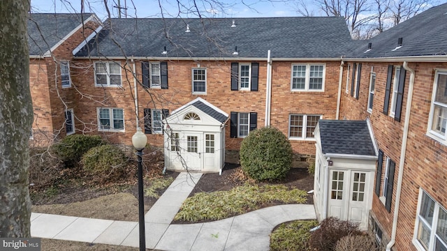 view of property featuring brick siding and roof with shingles