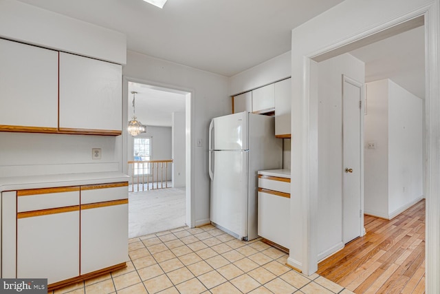 kitchen with baseboards, white cabinets, freestanding refrigerator, light countertops, and a chandelier