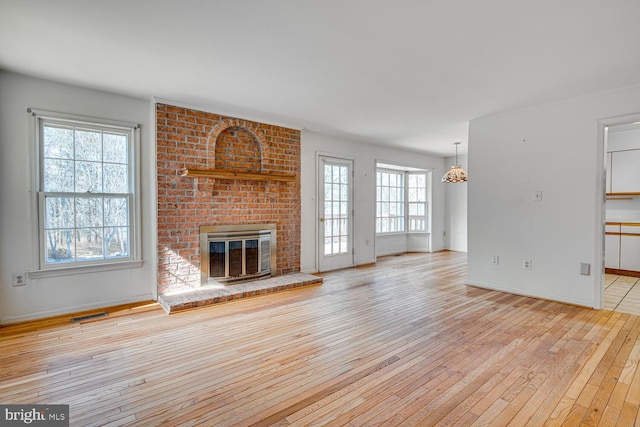 unfurnished living room featuring a chandelier, a fireplace, visible vents, baseboards, and light wood finished floors