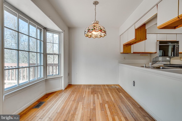 unfurnished dining area featuring a healthy amount of sunlight, light wood-style floors, baseboards, and visible vents