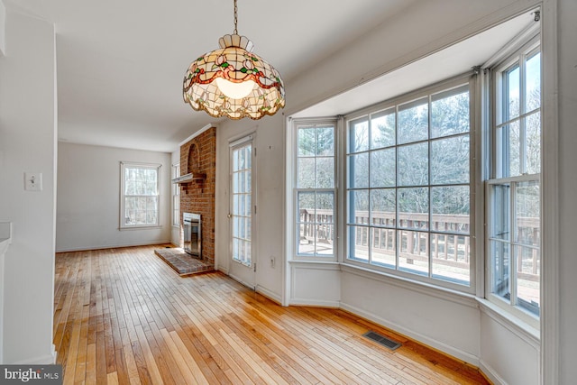 unfurnished living room with a brick fireplace, baseboards, visible vents, and hardwood / wood-style flooring