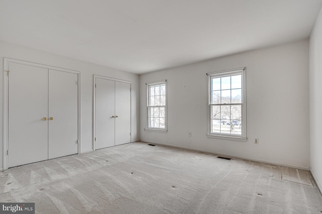 unfurnished bedroom with multiple closets, carpet flooring, visible vents, and baseboards