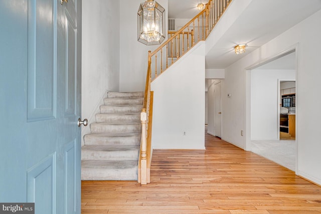 stairs with a notable chandelier, a towering ceiling, baseboards, and wood finished floors