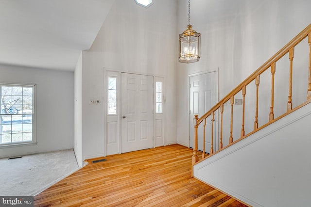 foyer with light wood finished floors, visible vents, a high ceiling, a chandelier, and stairs