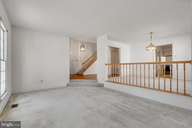 carpeted spare room with a chandelier, visible vents, stairway, and baseboards