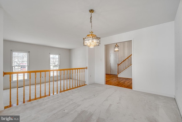 carpeted empty room with a chandelier and baseboards