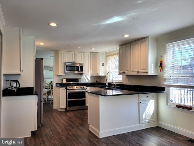 kitchen with dark countertops, dark wood-type flooring, a peninsula, stainless steel appliances, and a sink