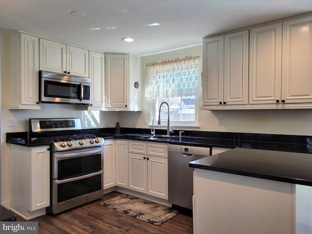 kitchen featuring dark countertops, dark wood-style flooring, stainless steel appliances, white cabinetry, and a sink