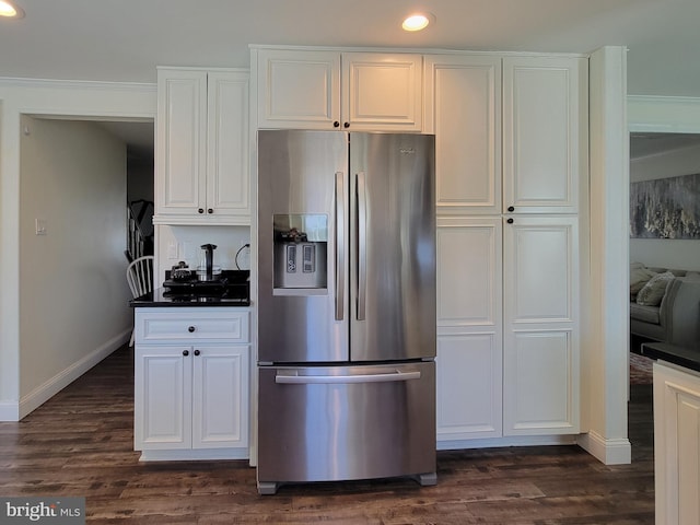 kitchen with dark wood-style flooring, dark countertops, white cabinets, stainless steel fridge, and baseboards