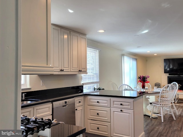 kitchen featuring white cabinets, dark countertops, a peninsula, stainless steel dishwasher, and a sink