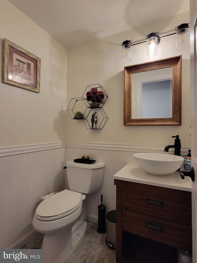 half bathroom with a wainscoted wall, vanity, toilet, and wood finished floors