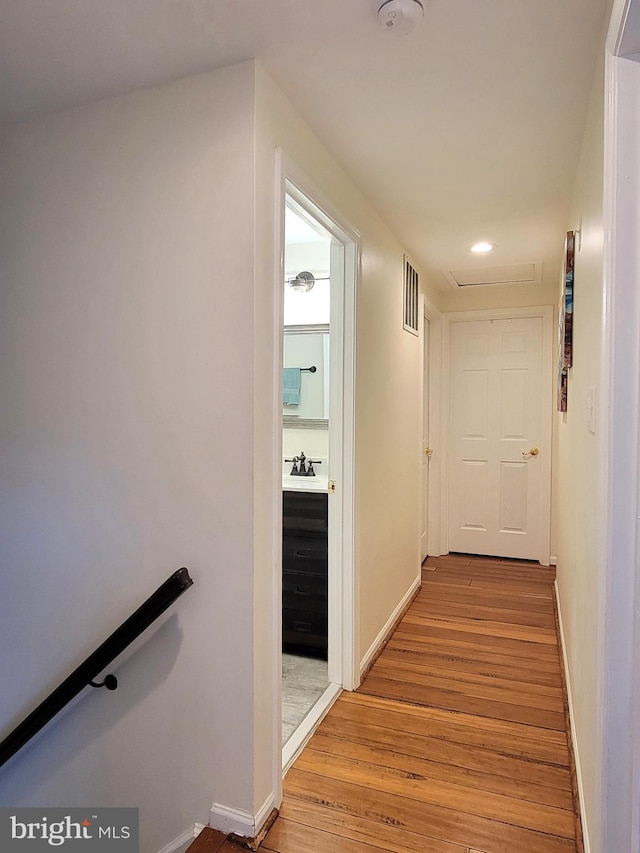 corridor featuring an upstairs landing, light wood-type flooring, visible vents, and baseboards