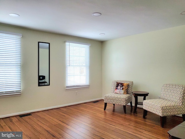 sitting room with wood-type flooring, visible vents, and baseboards