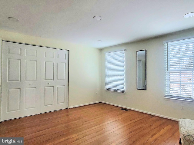 unfurnished bedroom featuring light wood-type flooring, a closet, visible vents, and baseboards