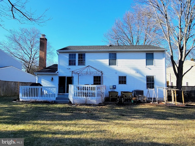 back of house featuring a yard, a chimney, a wooden deck, and fence