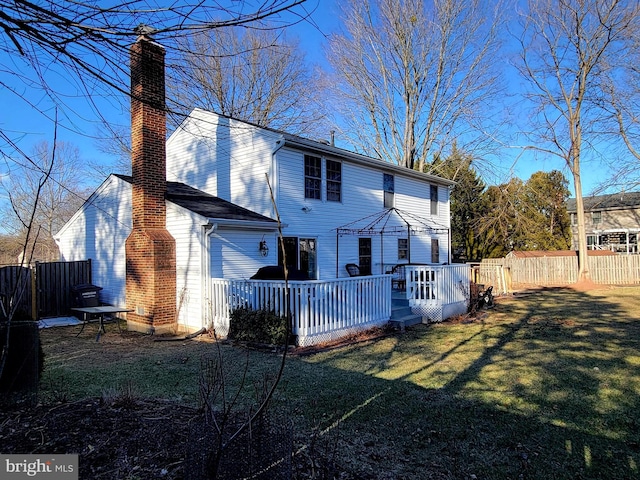 rear view of house featuring a deck, a chimney, fence, and a lawn