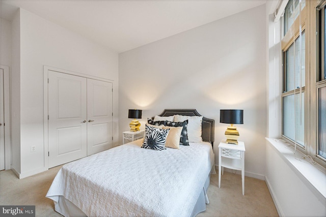 bedroom with baseboards, a closet, and light colored carpet