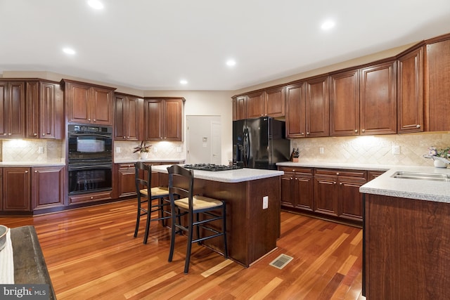 kitchen with a kitchen island, a kitchen breakfast bar, wood finished floors, black appliances, and a sink