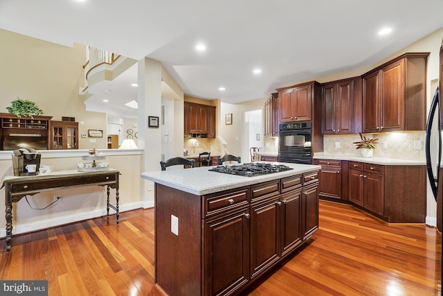 kitchen featuring light wood finished floors, stainless steel gas stovetop, dobule oven black, and light countertops