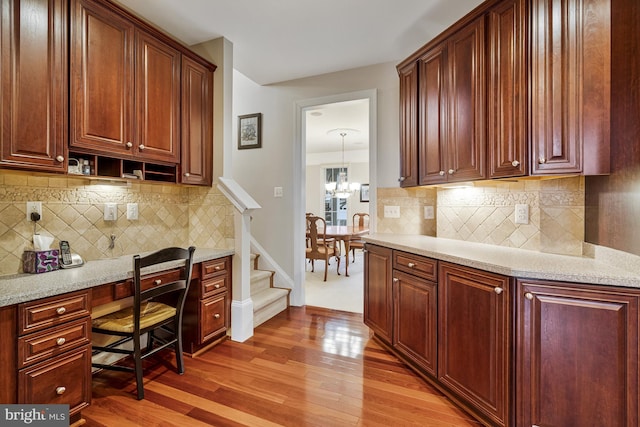 kitchen featuring backsplash, a notable chandelier, light wood finished floors, and built in study area