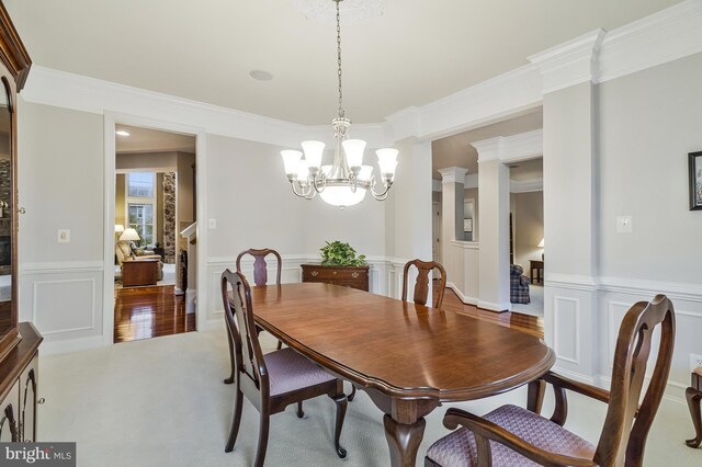 carpeted dining room featuring a wainscoted wall, decorative columns, crown molding, and a decorative wall