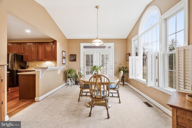 dining room with light tile patterned floors, visible vents, a healthy amount of sunlight, and lofted ceiling