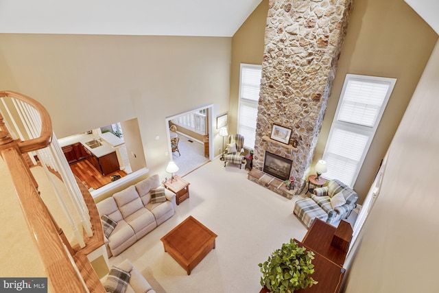 carpeted living room with a stone fireplace and high vaulted ceiling