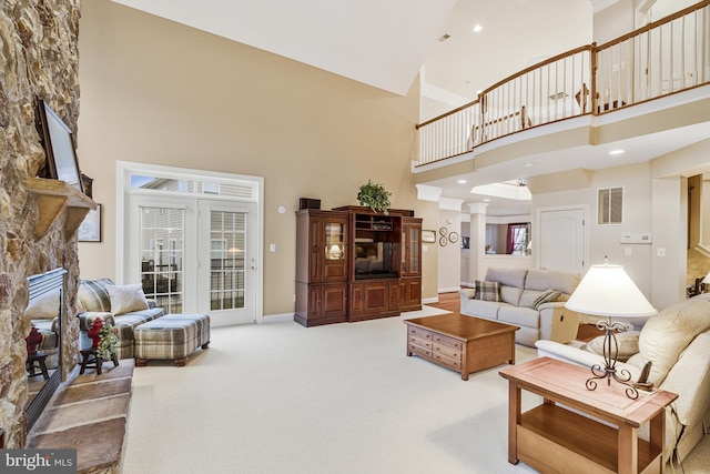 carpeted living area with visible vents, a high ceiling, a fireplace, decorative columns, and baseboards