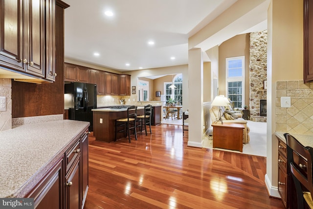 kitchen featuring dark wood finished floors, decorative backsplash, black fridge, and a breakfast bar area