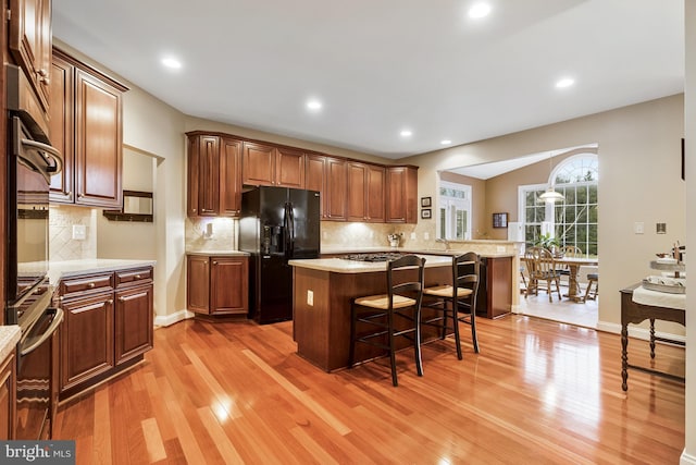 kitchen with black fridge, a kitchen breakfast bar, wall oven, light wood finished floors, and light countertops