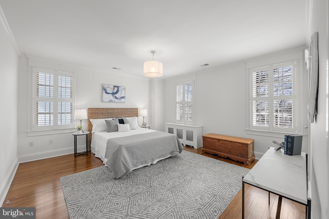 bedroom with baseboards, wood-type flooring, visible vents, and crown molding