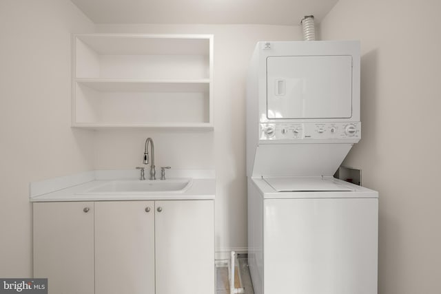 clothes washing area with stacked washer / dryer, cabinet space, and a sink