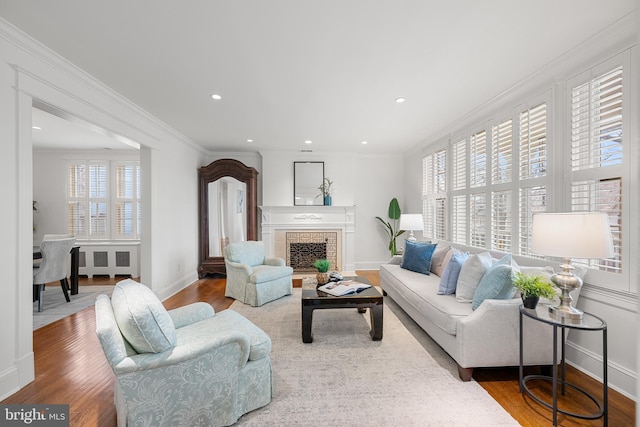 living area featuring radiator heating unit, a fireplace, ornamental molding, and wood finished floors