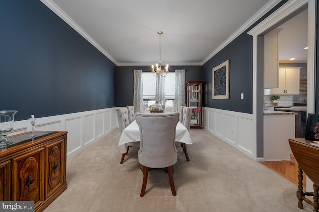 dining space featuring a chandelier, a decorative wall, ornamental molding, and light colored carpet