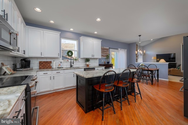 kitchen with light wood-style flooring, appliances with stainless steel finishes, a breakfast bar, white cabinetry, and a sink