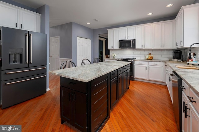 kitchen with tasteful backsplash, white cabinets, light wood-style flooring, stainless steel appliances, and a sink